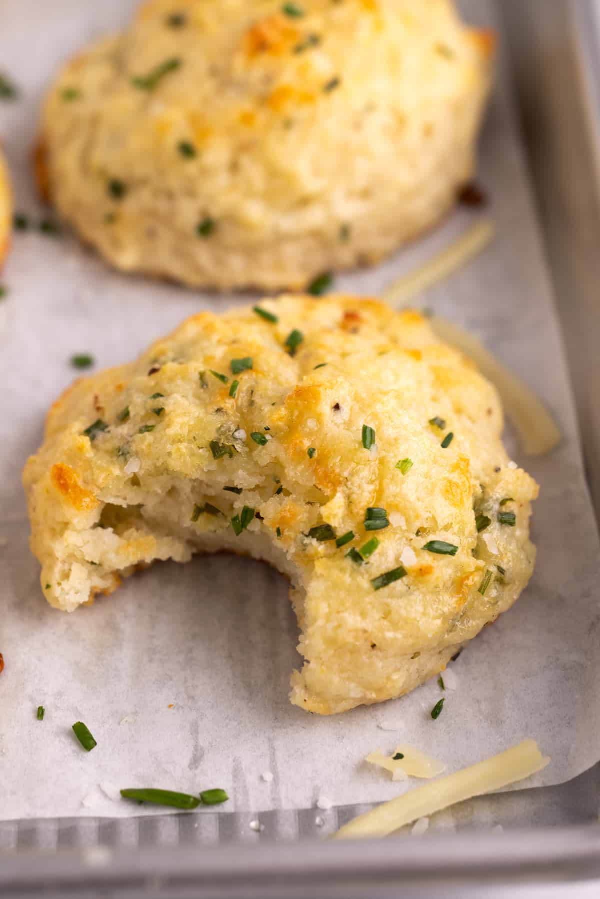 A cheddar chive biscuit with a bite taken out of it.