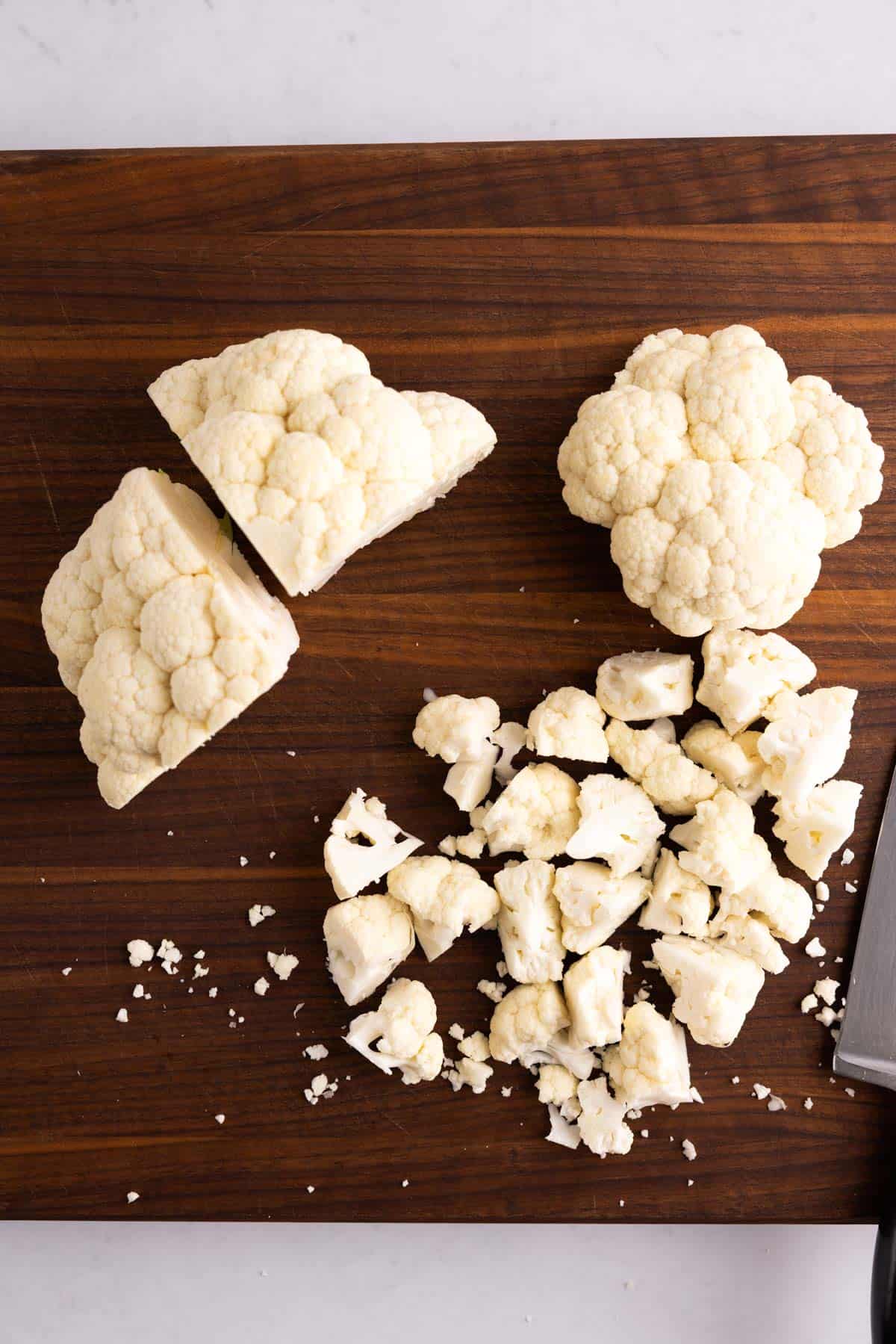 Raw chopped cauliflower on a wooden cutting board with a knife.
