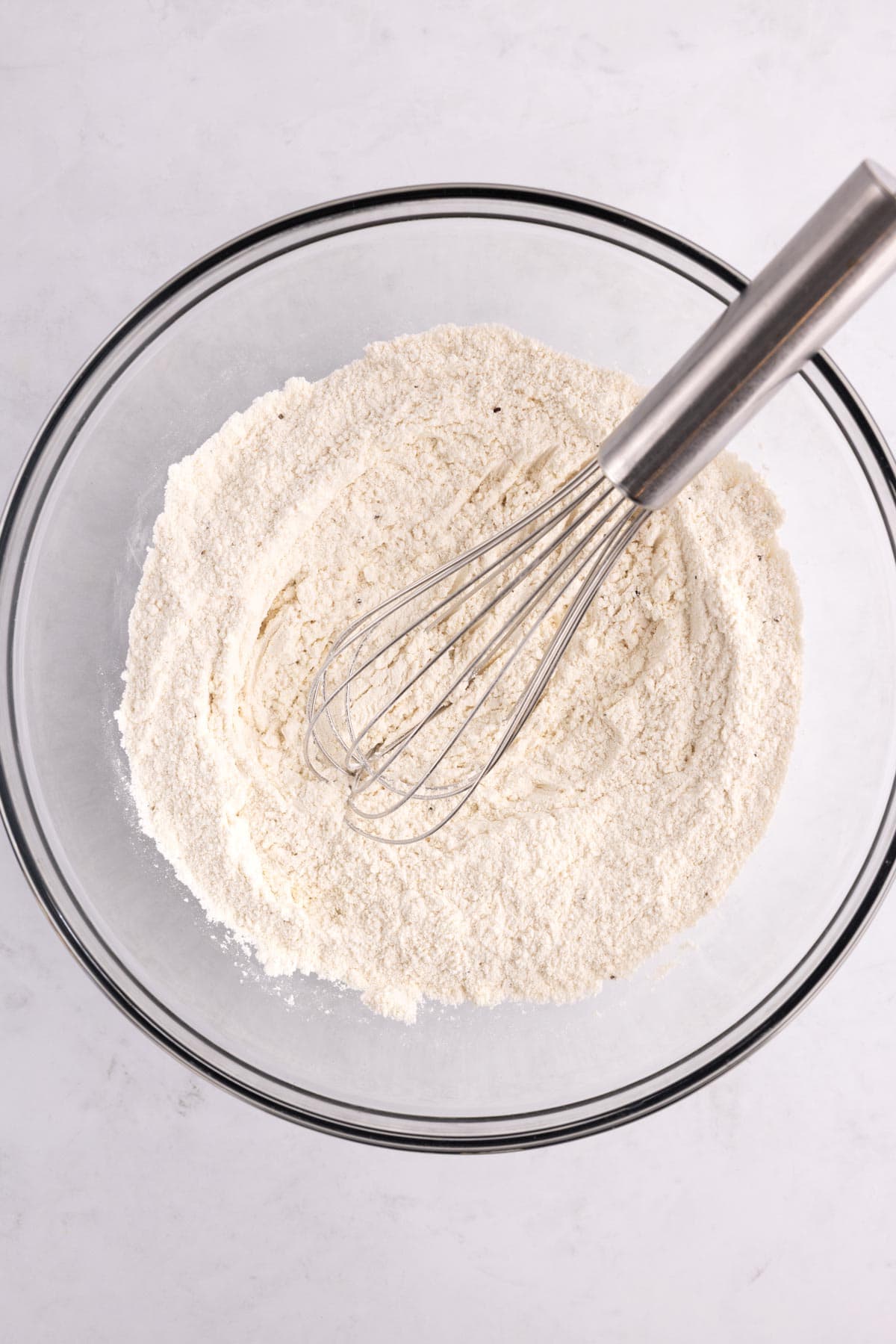 A whisk sitting in a bowl of combined dry ingredients.