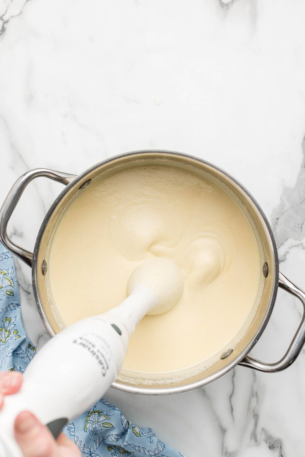 An immersion blender mixing the cheese sauce together in a pot.