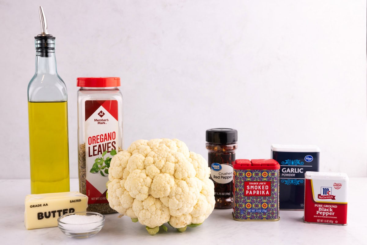 Oil, oregano, butter, salt, cauliflower, red pepper, paprika, garlic powder, and black pepper on a countertop.