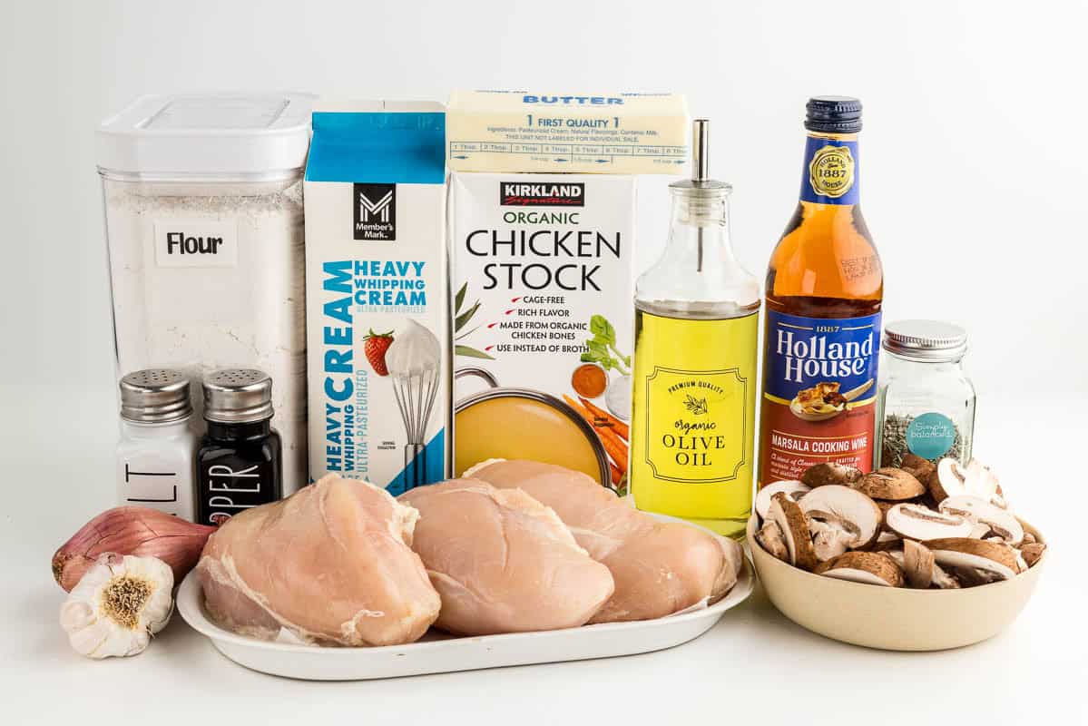 Flour, chicken, garlic, onion, mushrooms, heavy whipping cream, chicken stock, butter, oil, wine, and herbs on a white surface.