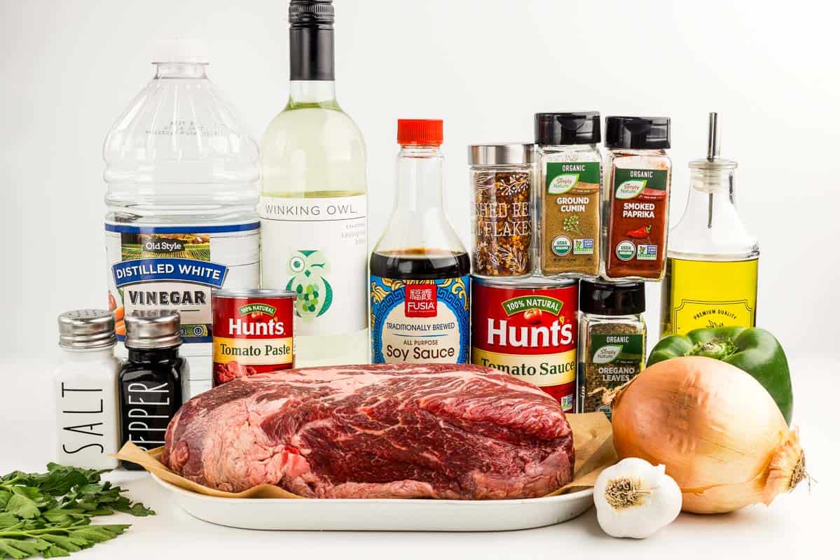 Garlic, beef, onion, bell pepper, oil tomato sauce, seasonings, salt and pepper, say sauce, tomato paste, wine, parsley, and vinegar on a counter.