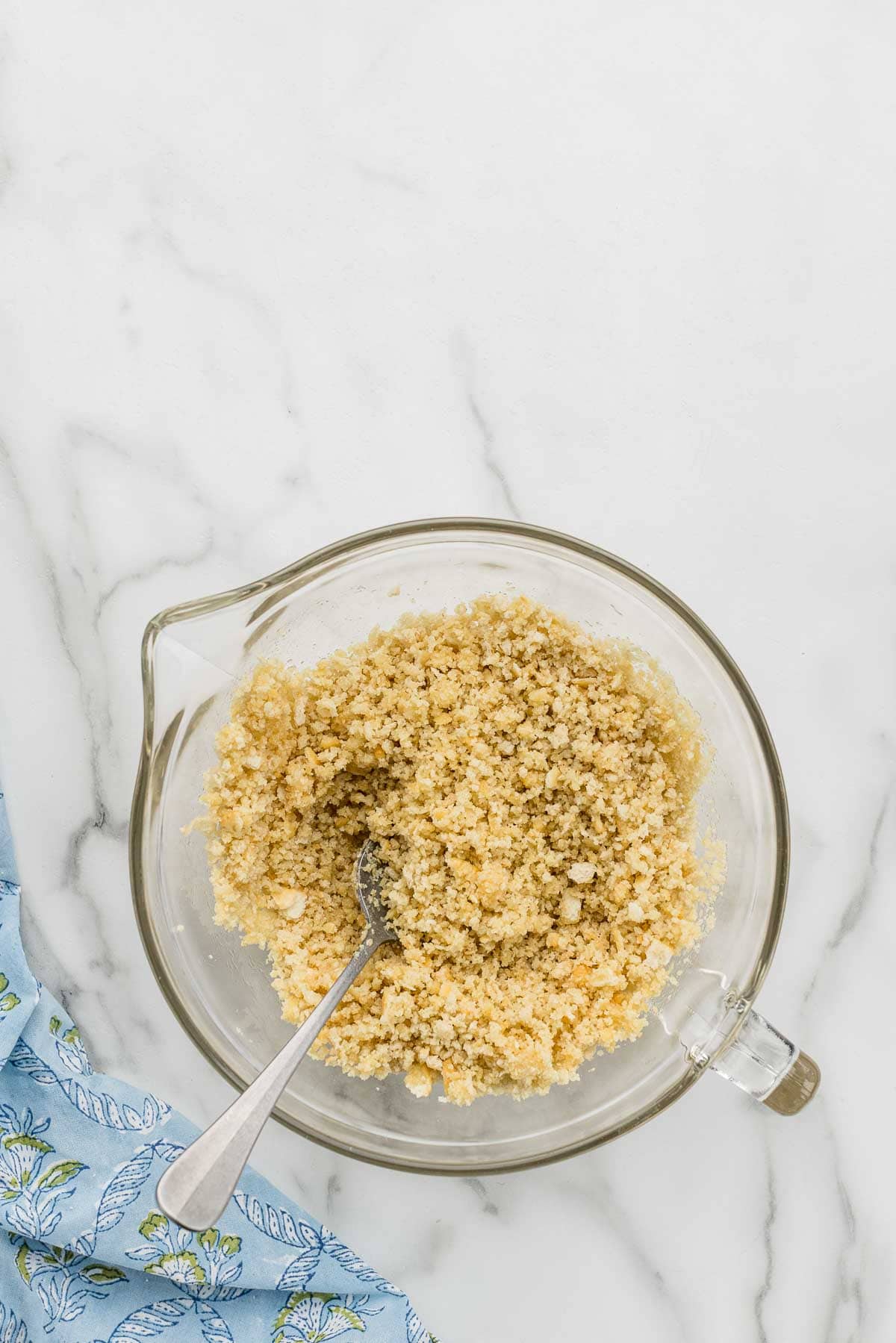 Breadcrumb topping mixed with a spoon in a glass measuring cup.