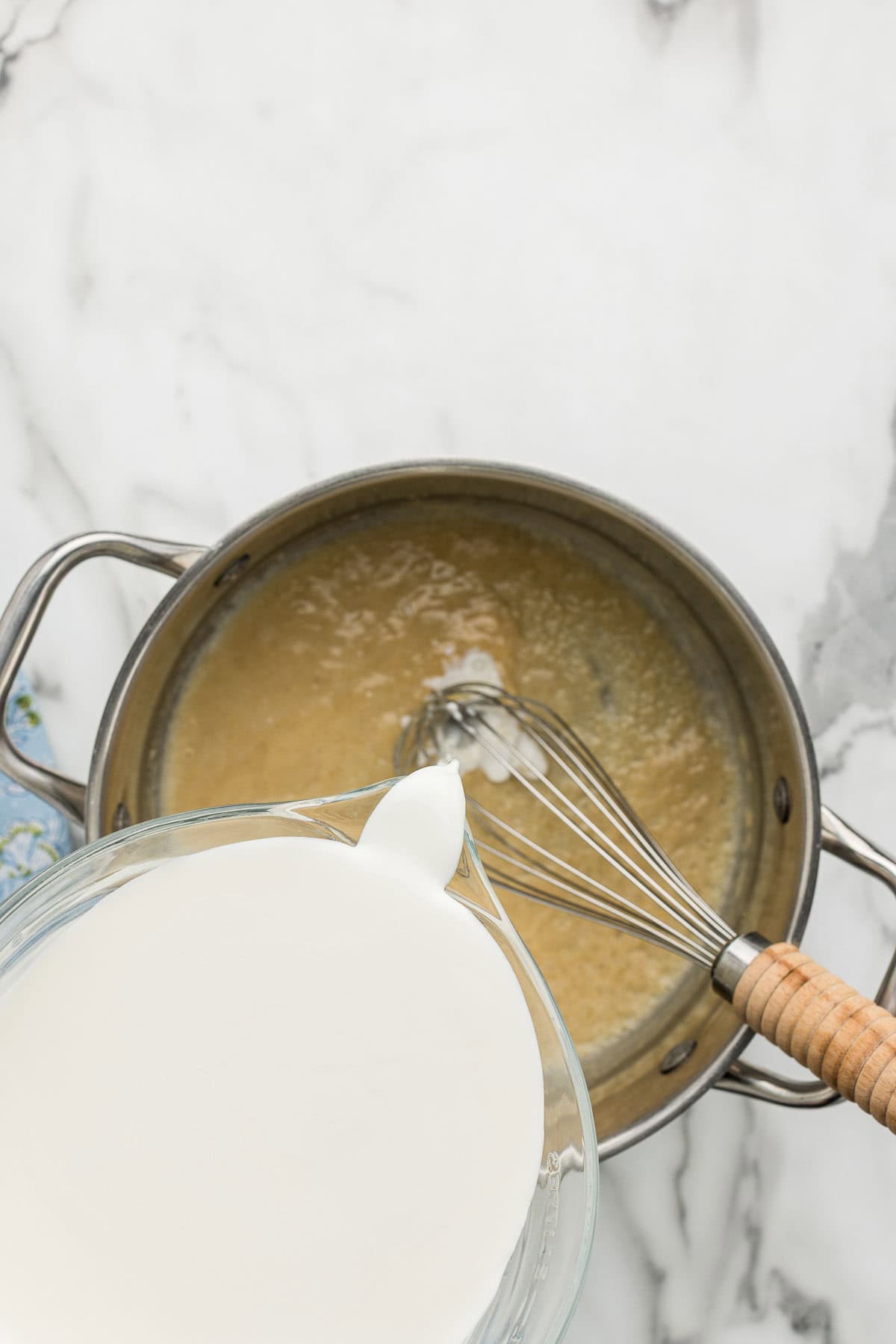 Pouring milk into a pot of cheese sauce with a whisk.