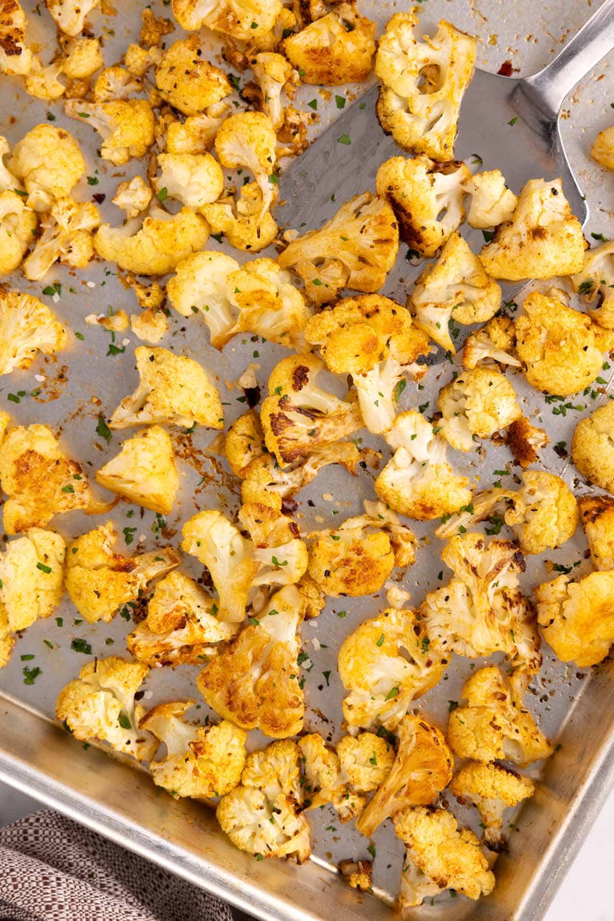 A spatula scooping cauliflower on a sheet pan.