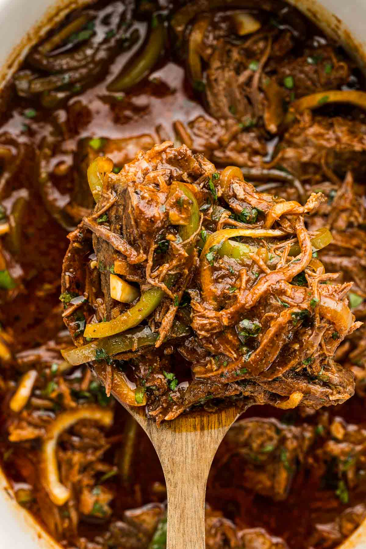 A spoonful of ropa vieja over a crock pot.