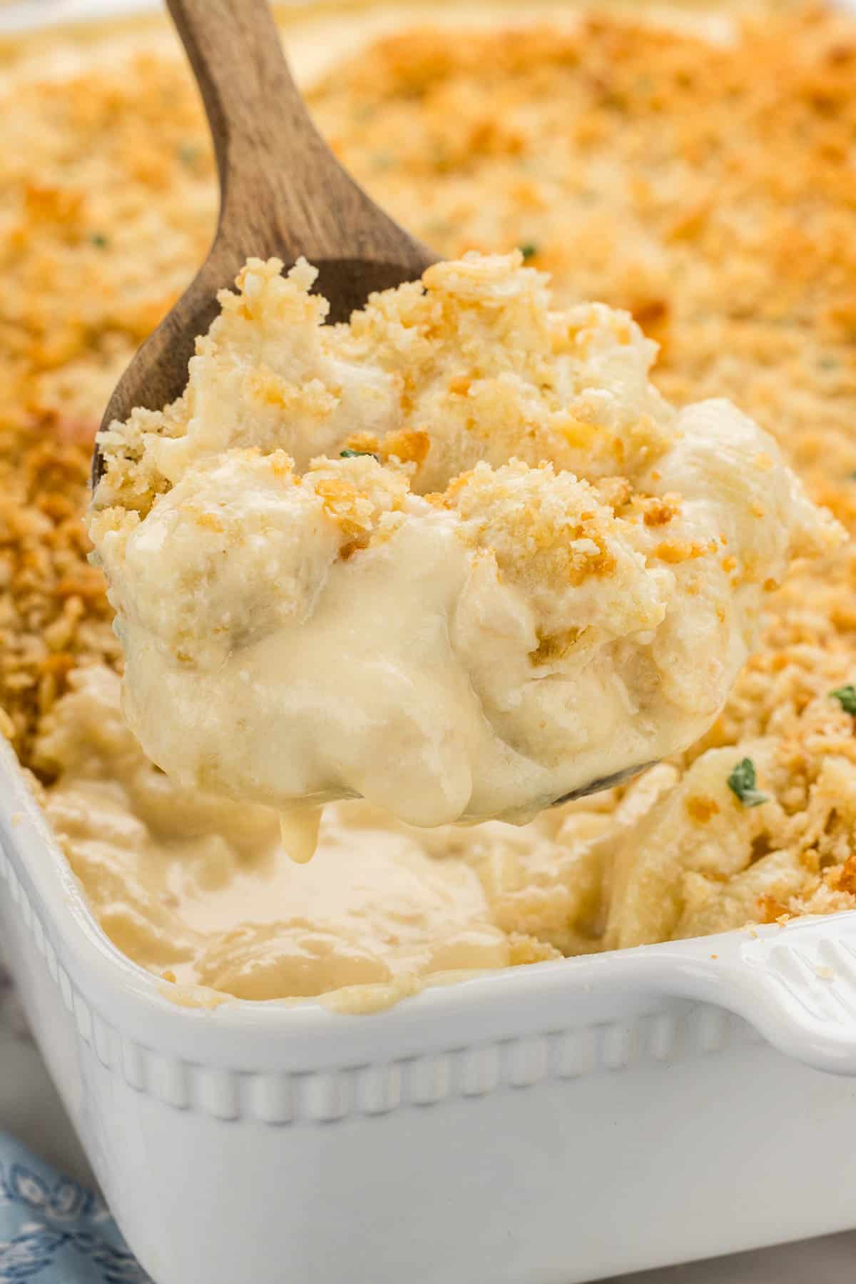 A spoonful of mac and cheese hovering over a white baking pan.