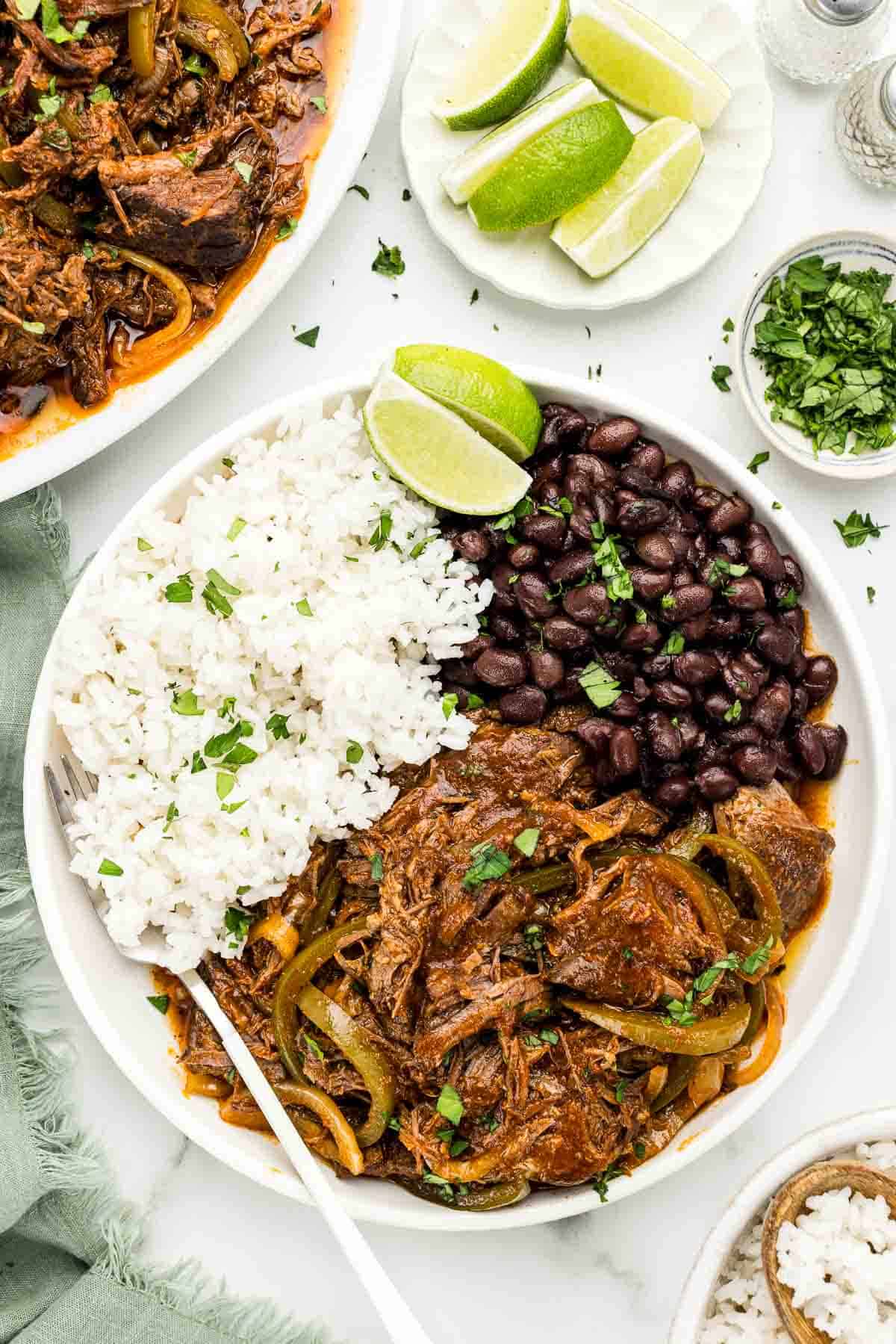 A serving of ropa vieja on a white plate with a fork.