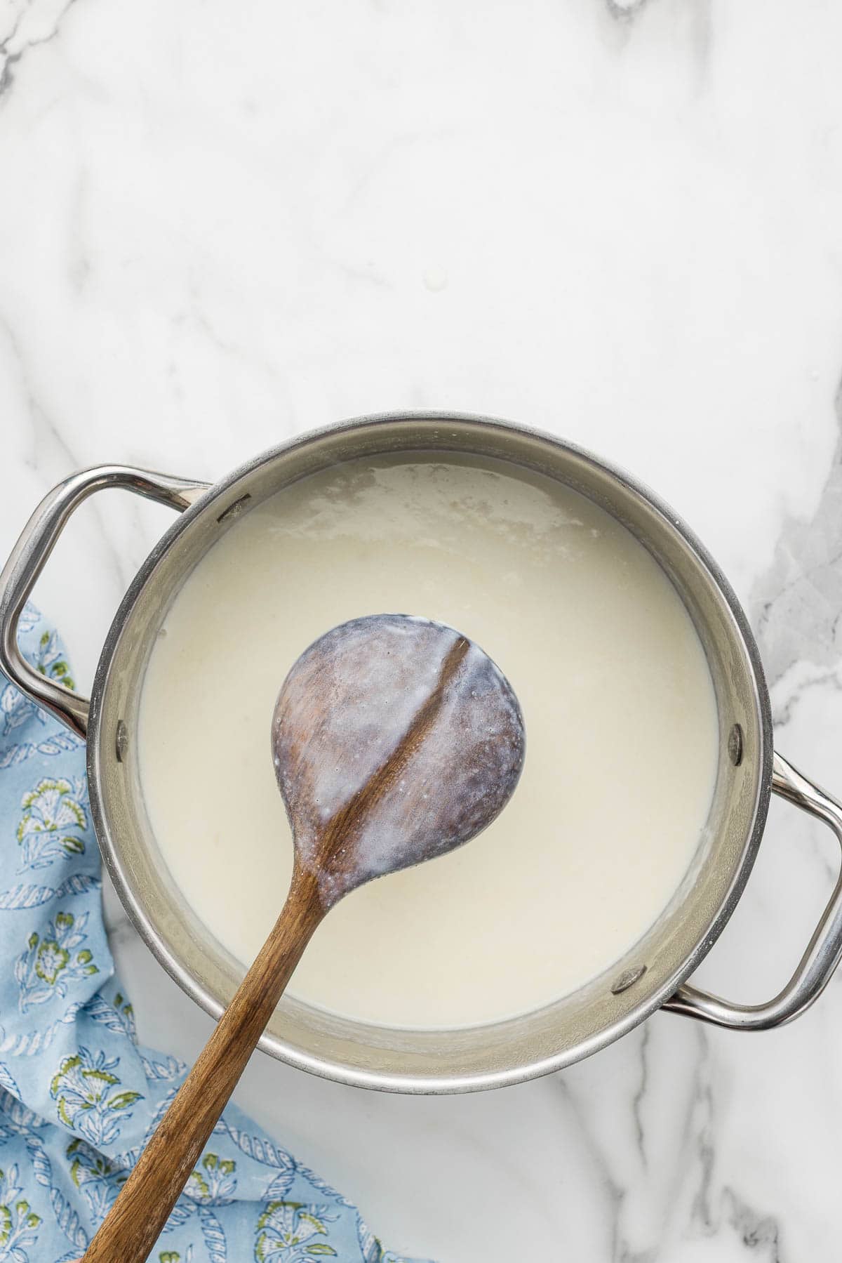 A wooden spoon over a pot of cheese sauce.