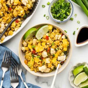 A bowl of pineapple rice with a fork and an array of ingriedients around it.