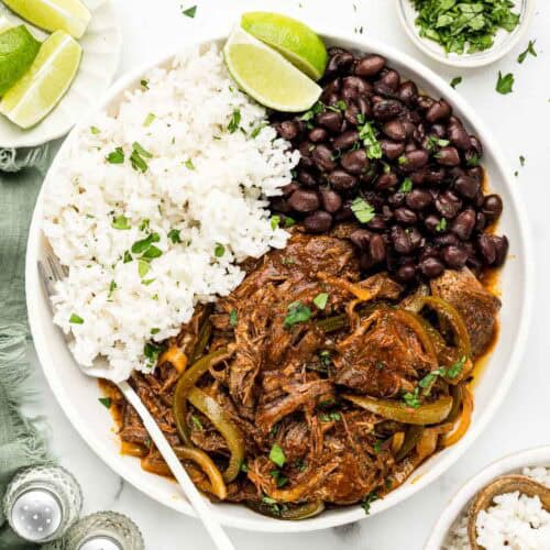 Rice, beans, and ropa vieja on a white dish with a fork.