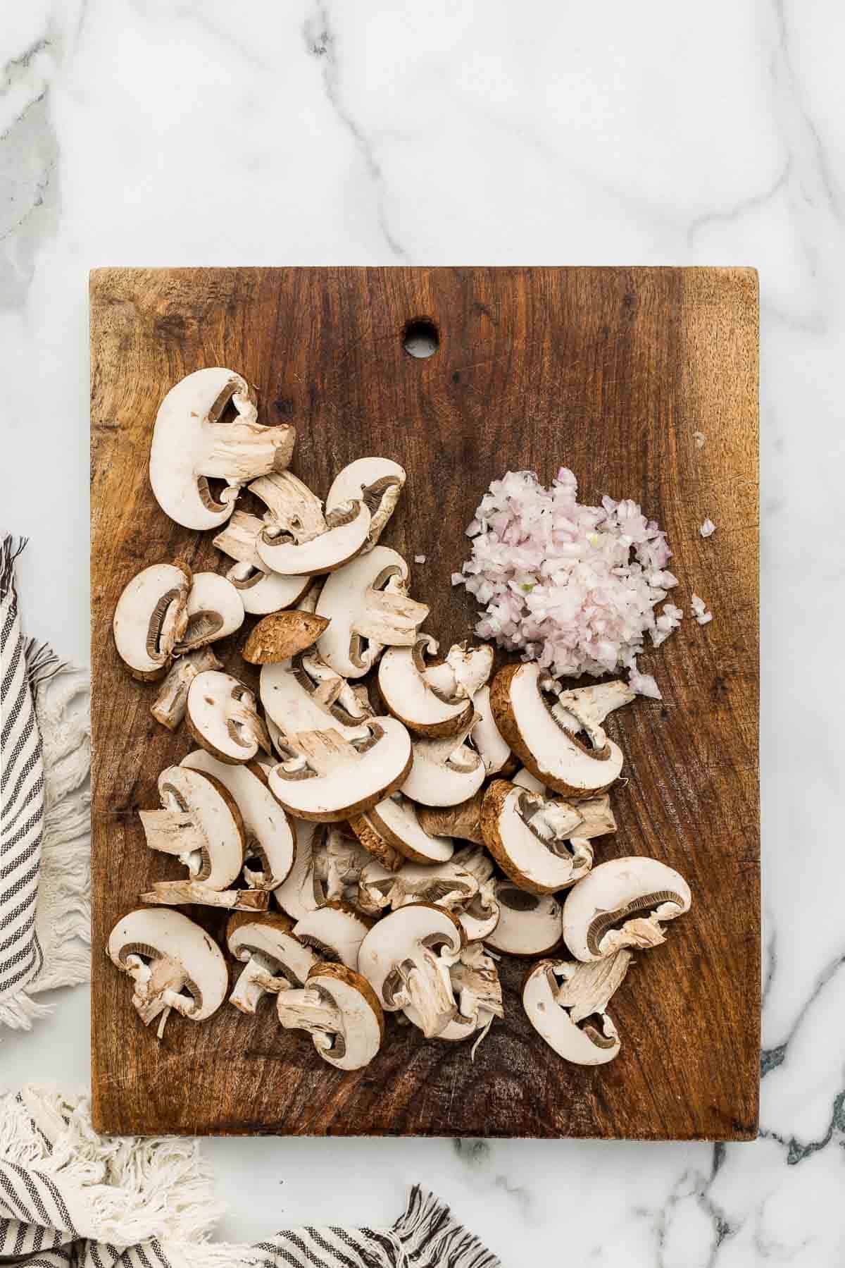 Mushrooms and onion on a cutting board.