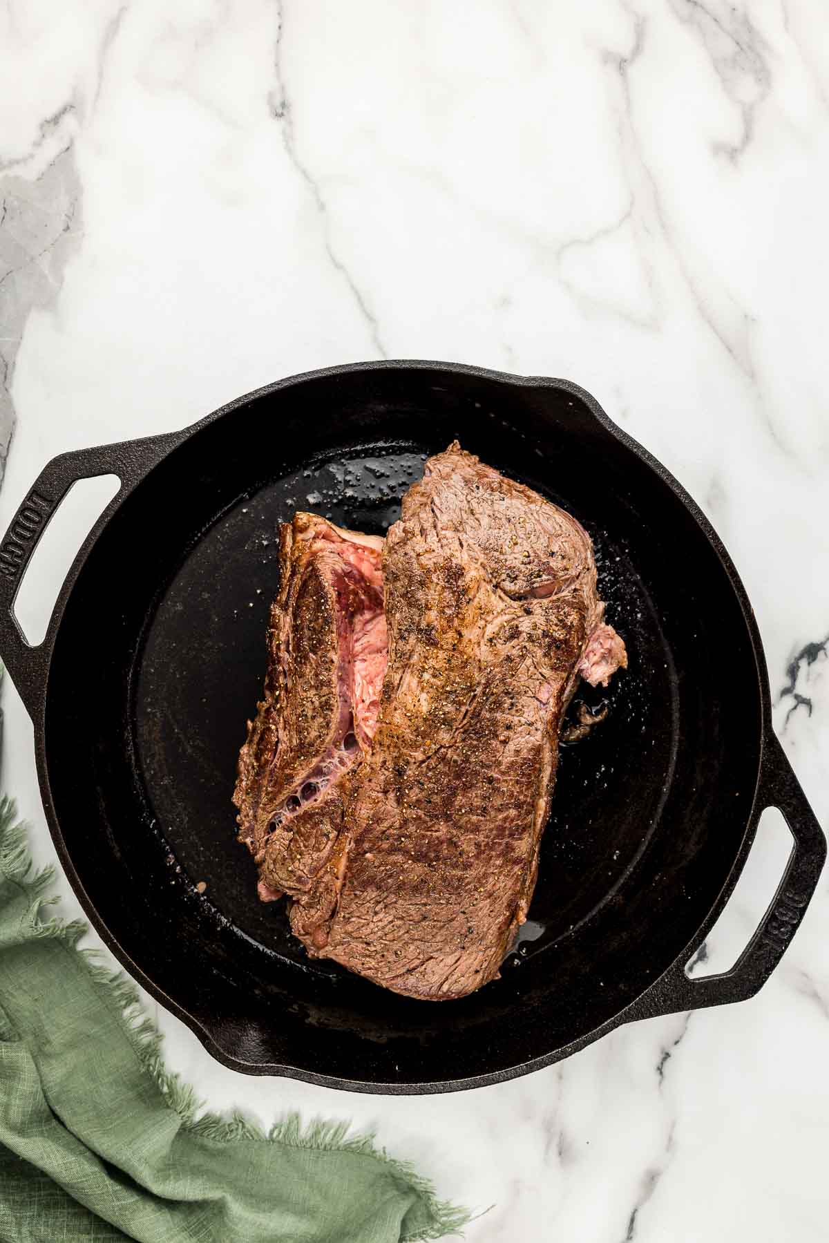 Chuck roast cooking on a cast iron skillet.