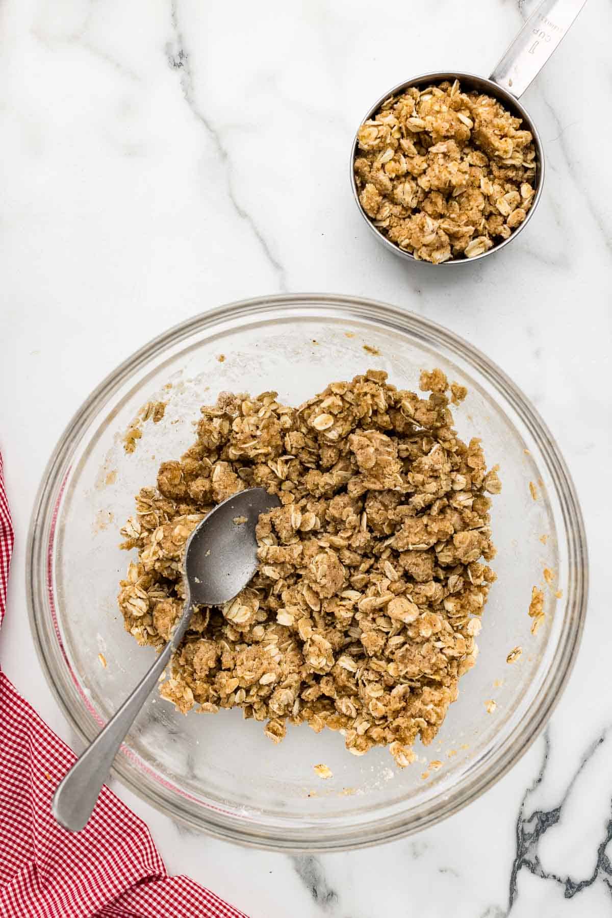 Oat crumble mixture in a glass mixing bowl with a spoon.