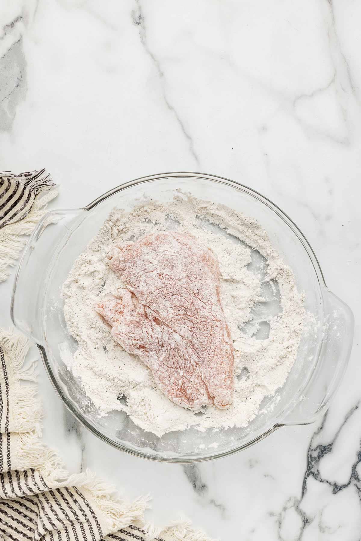 Raw chicken coated in a dish of flour mixture.