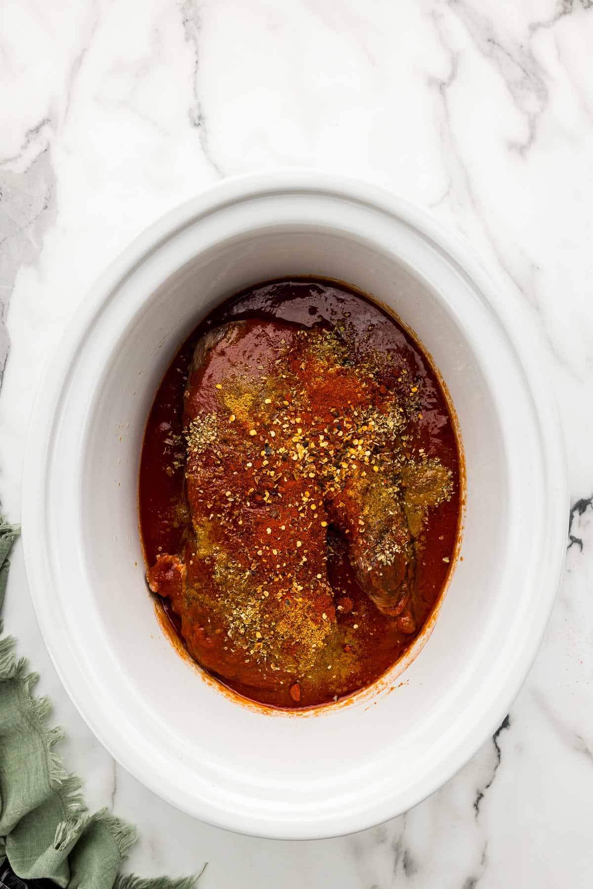 Seasoned meat and sauce in a crock pot.