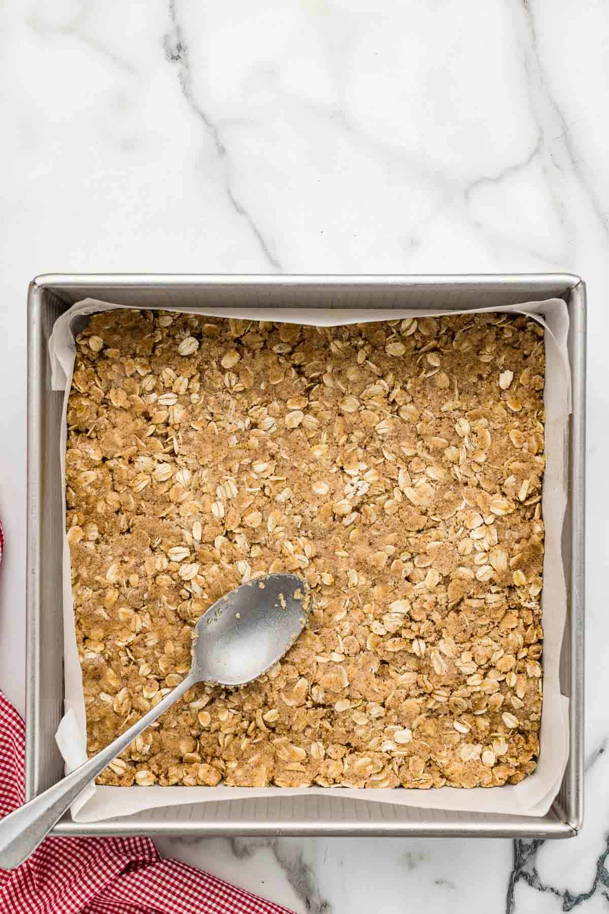 Crumble topping being pressed into a baking pan with a spoon.