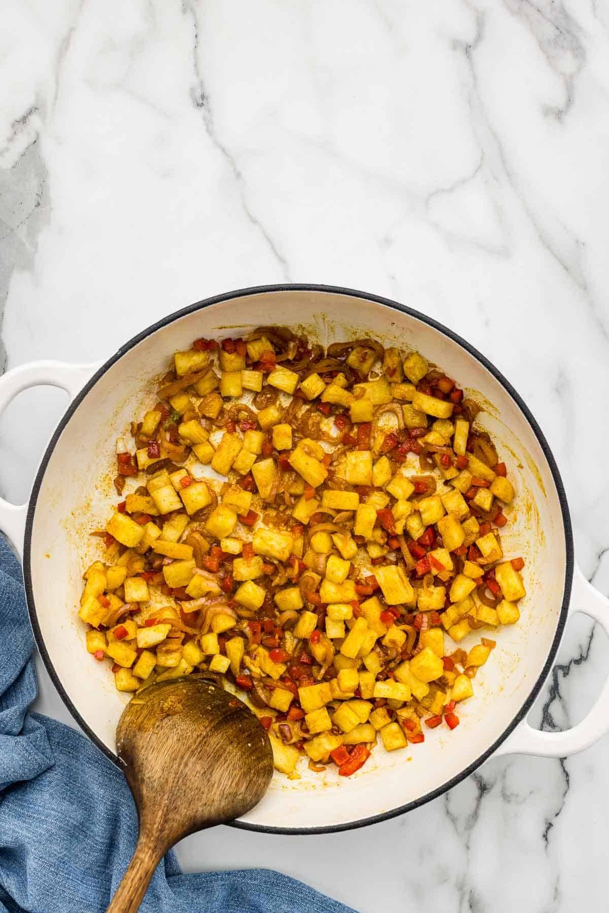 Veggies and pineapple cooking in a large pan with a wooden spoon.