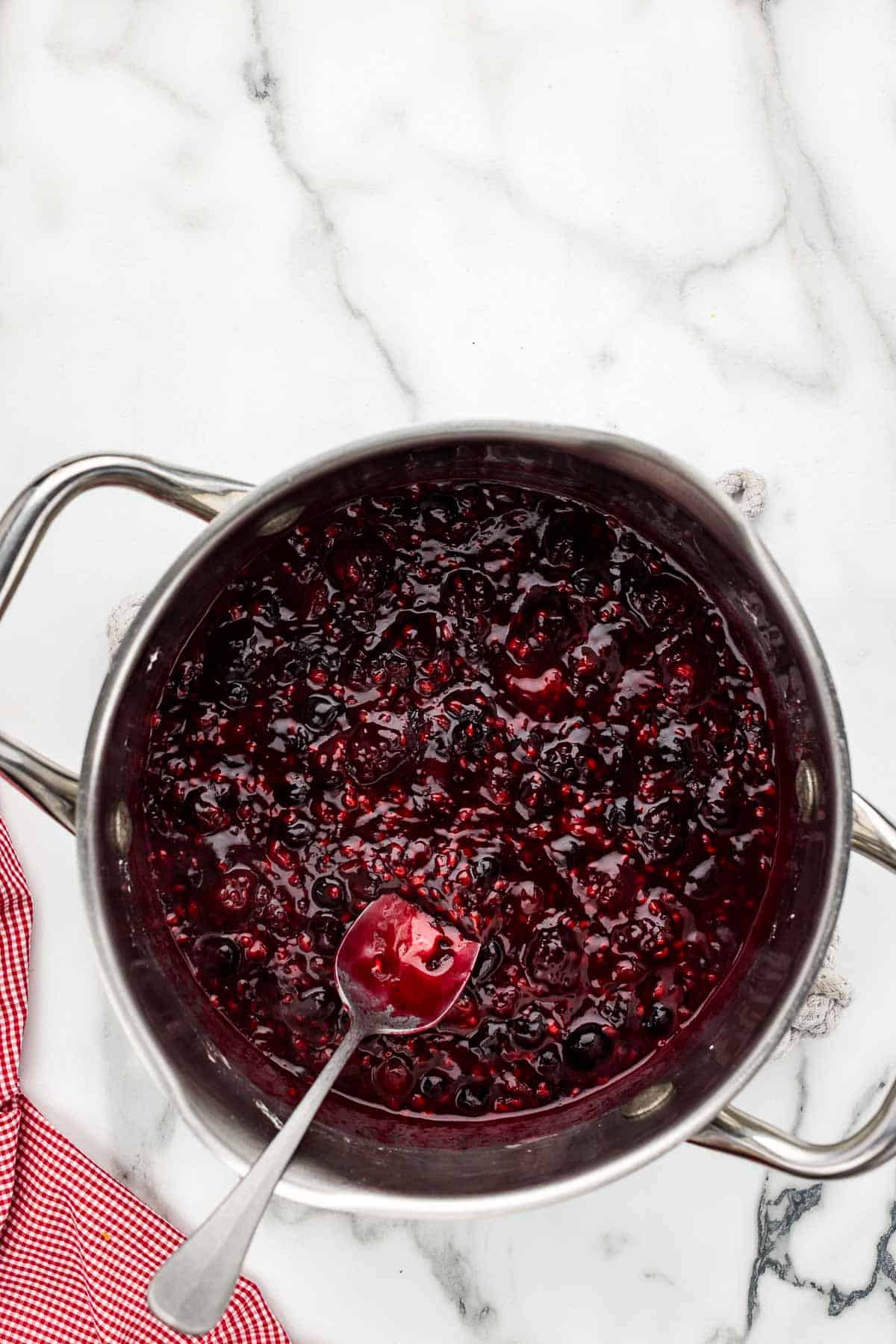 Berry mixture in a saucepan with a spoon.
