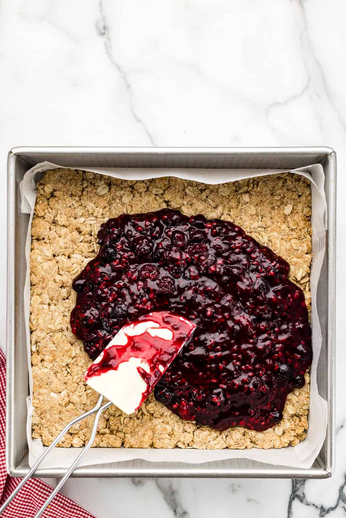 Pouring berry mixture into a square pan with a spatula.