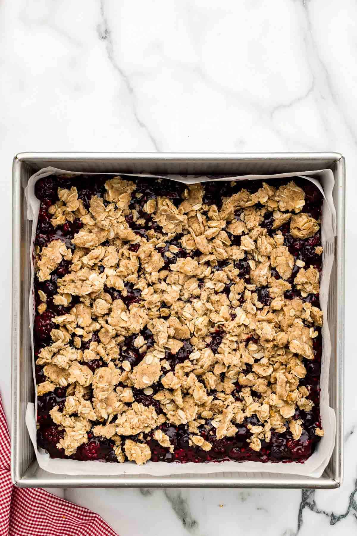 Oat crumble sprinkled on top of a pan of uncooked berry bars.