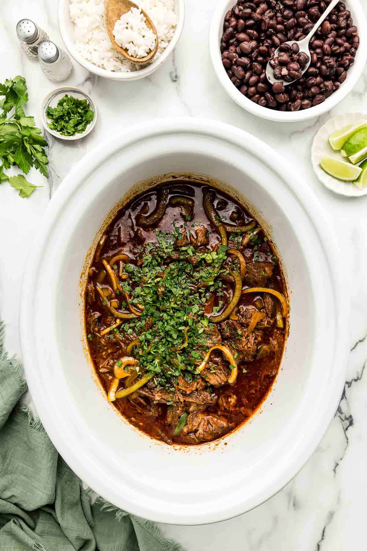 Parsley added to a slow cooker full of meat and juices.