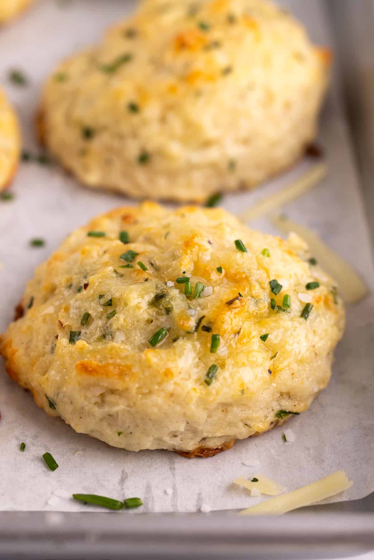 A cheddar chive biscuit sprinkled with chives on a sheet pan.