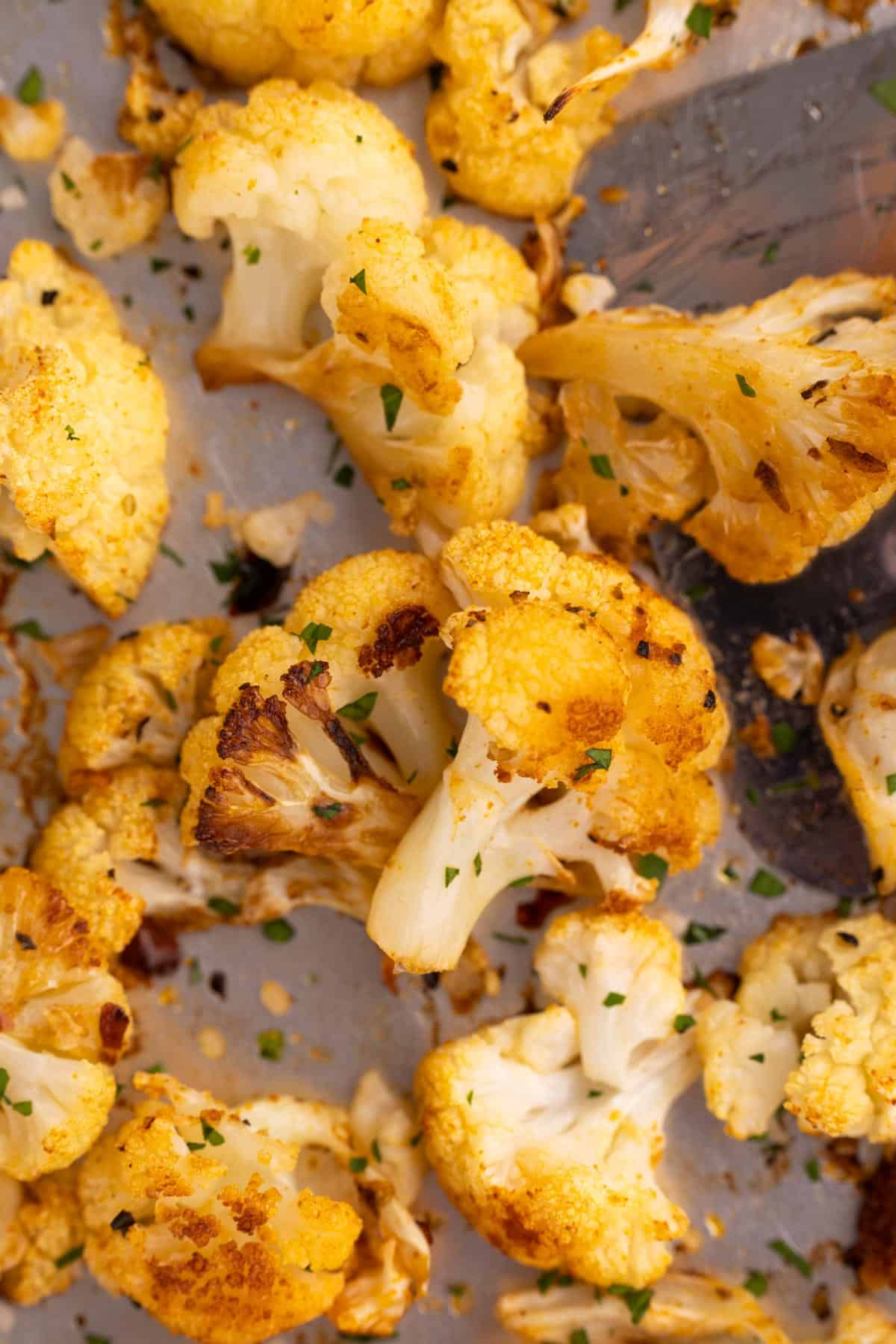 A piece of cauliflower on a sheet pan with a serving spatula beside it.