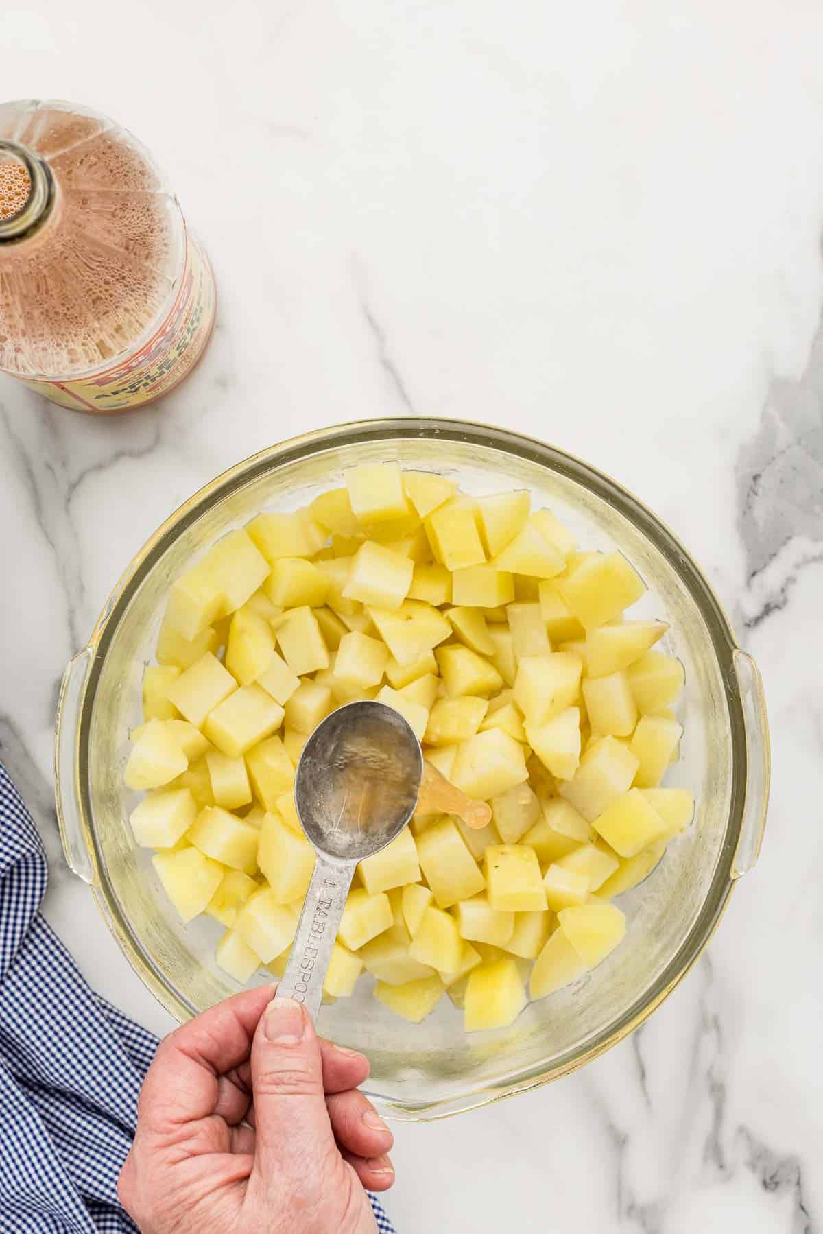 A tablespoon being held over a bowl of potatoes.