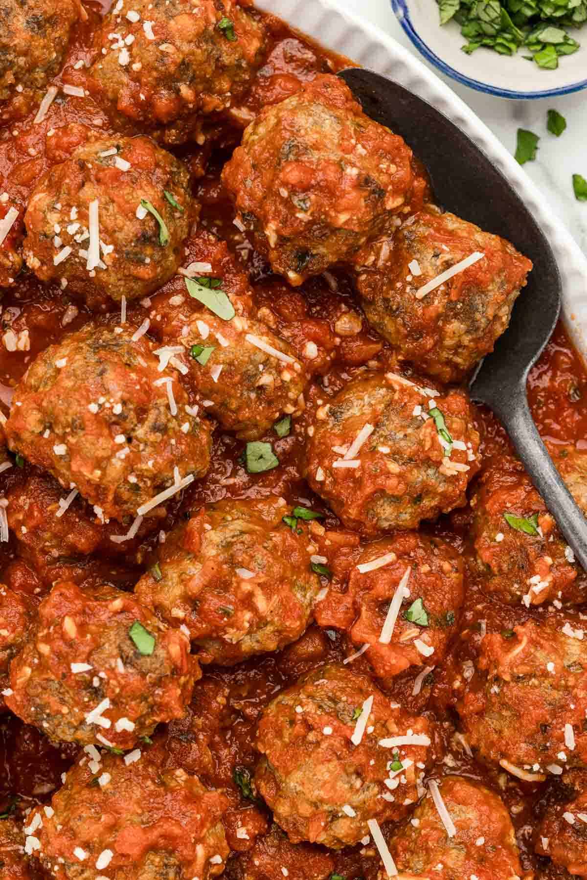 A large serving plate full of Italian meatballs with a spoon.