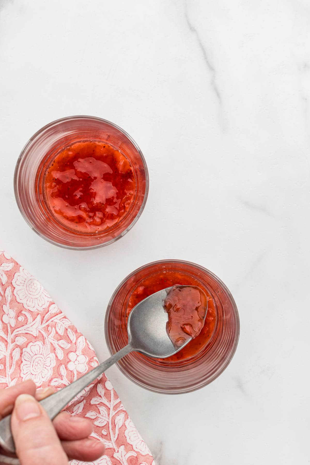 A spoon in a serving glass of strawberry sauce.