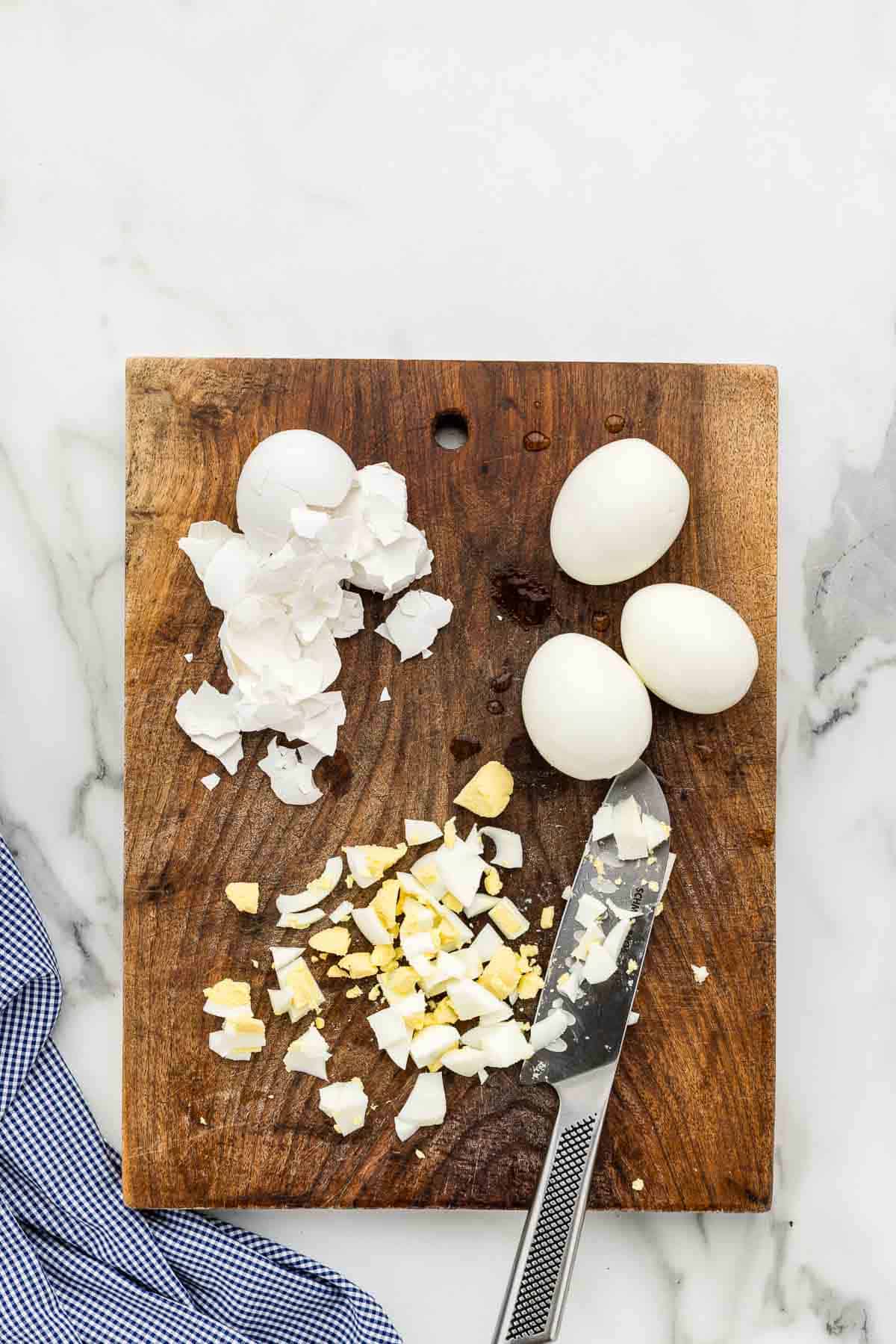 Eggs being chopped with a large knife on a wooden cutting board.