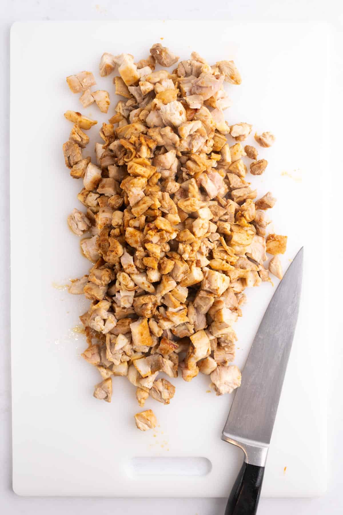 Chicken chopped up on a white cutting board with a knife.