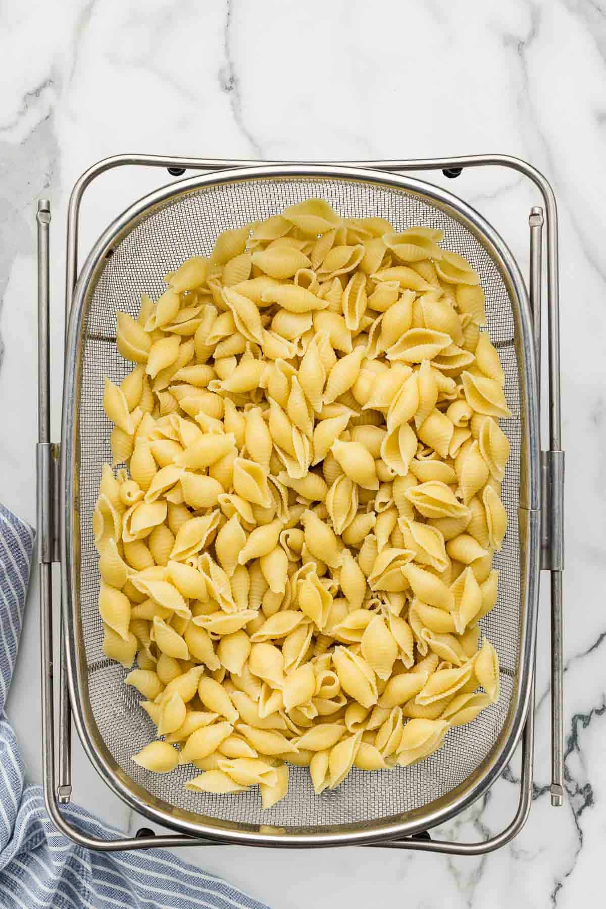 Shell pasta being drained in a strainer.