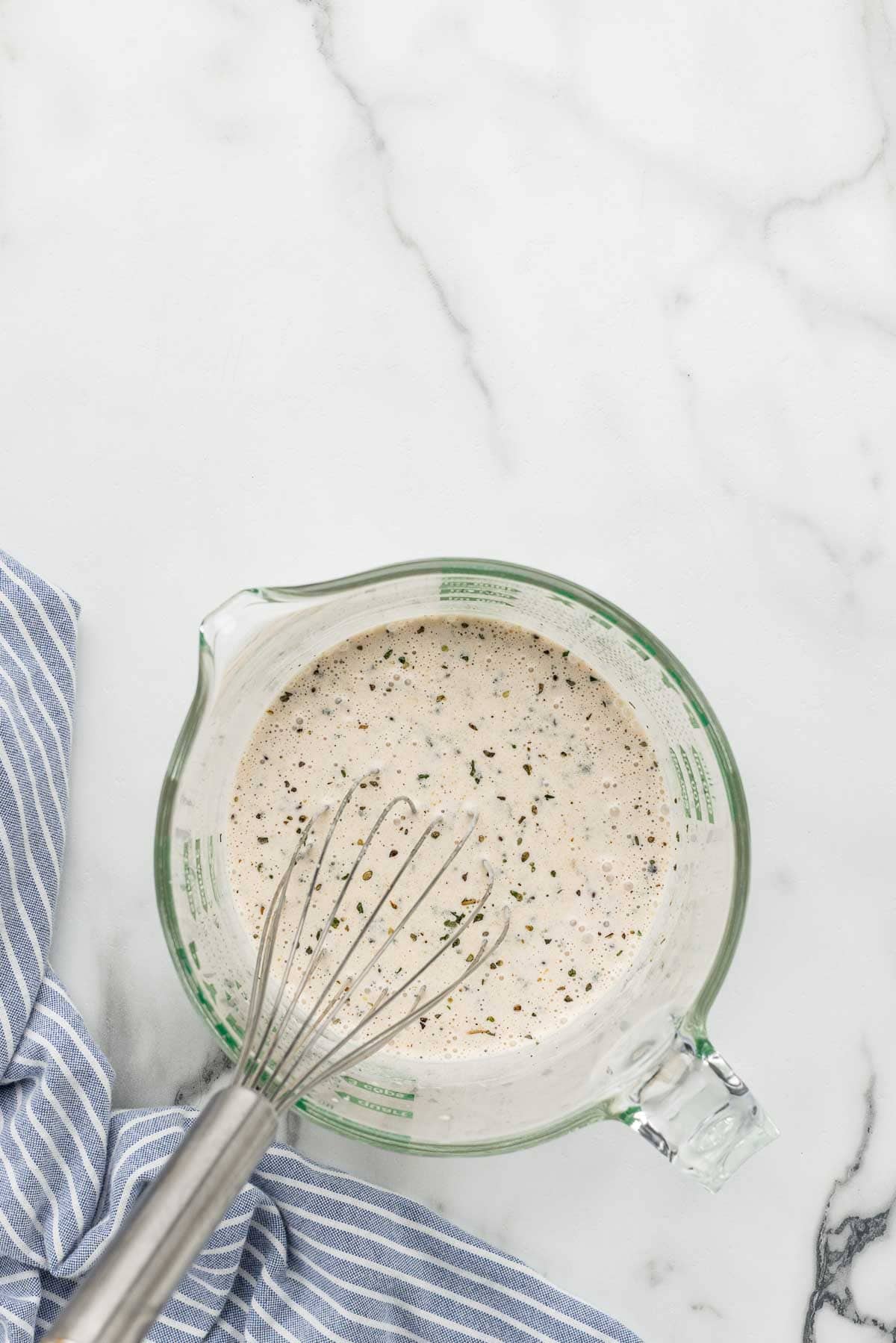 Creamy dressing mixed with a whisk in a glass dish.