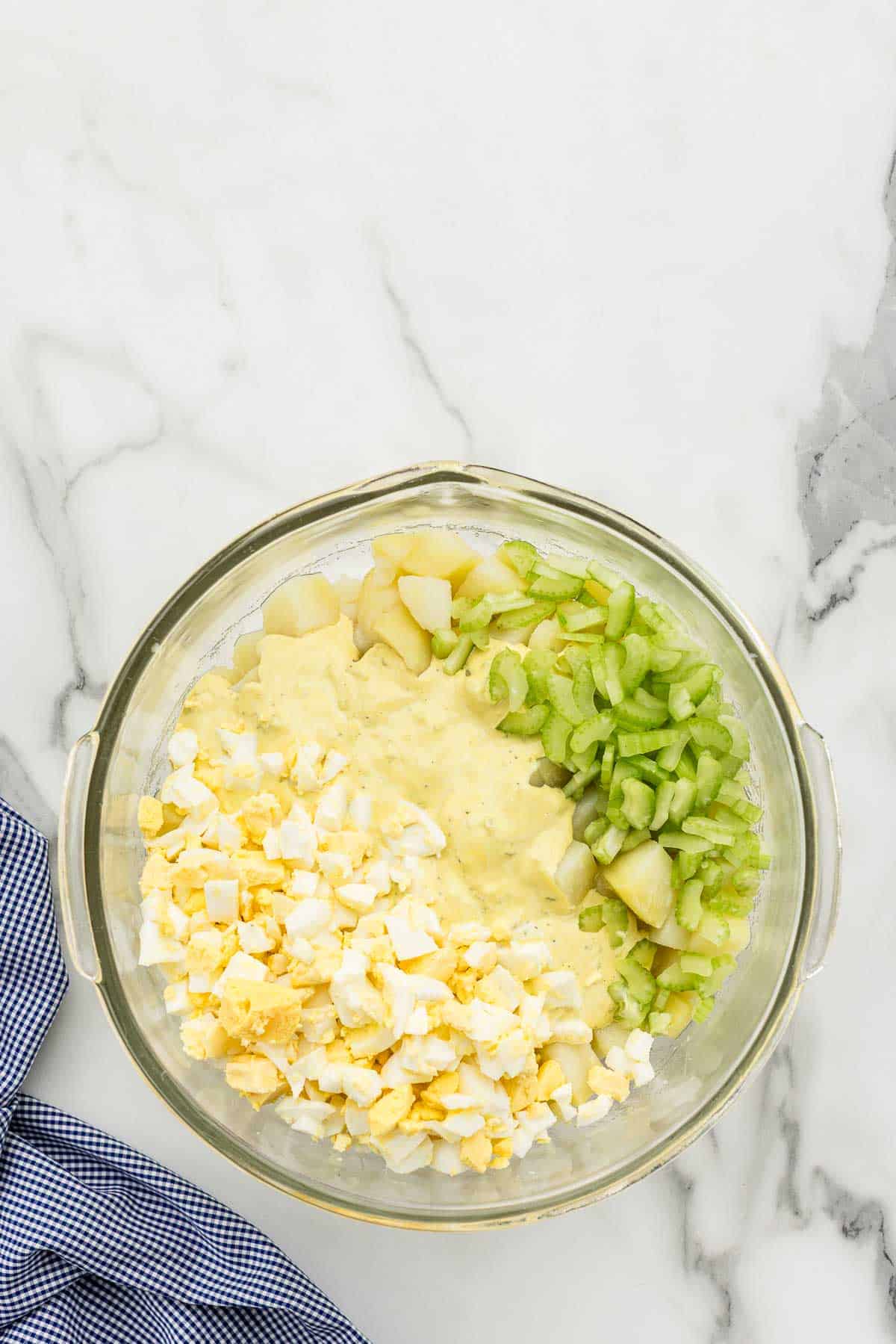 Potato salad ingredients in a large glass mixing bowl.