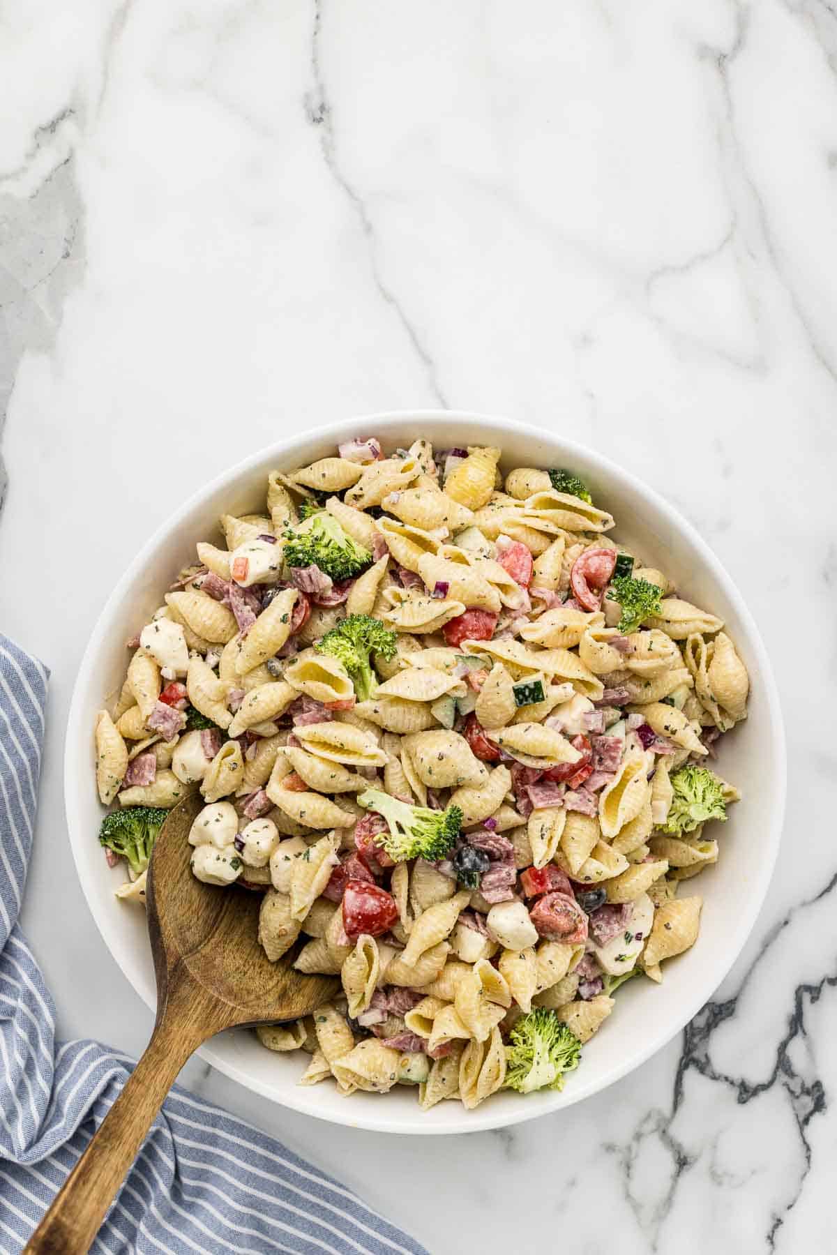 A bowl of creamy pasta salad with a wooden spoon.