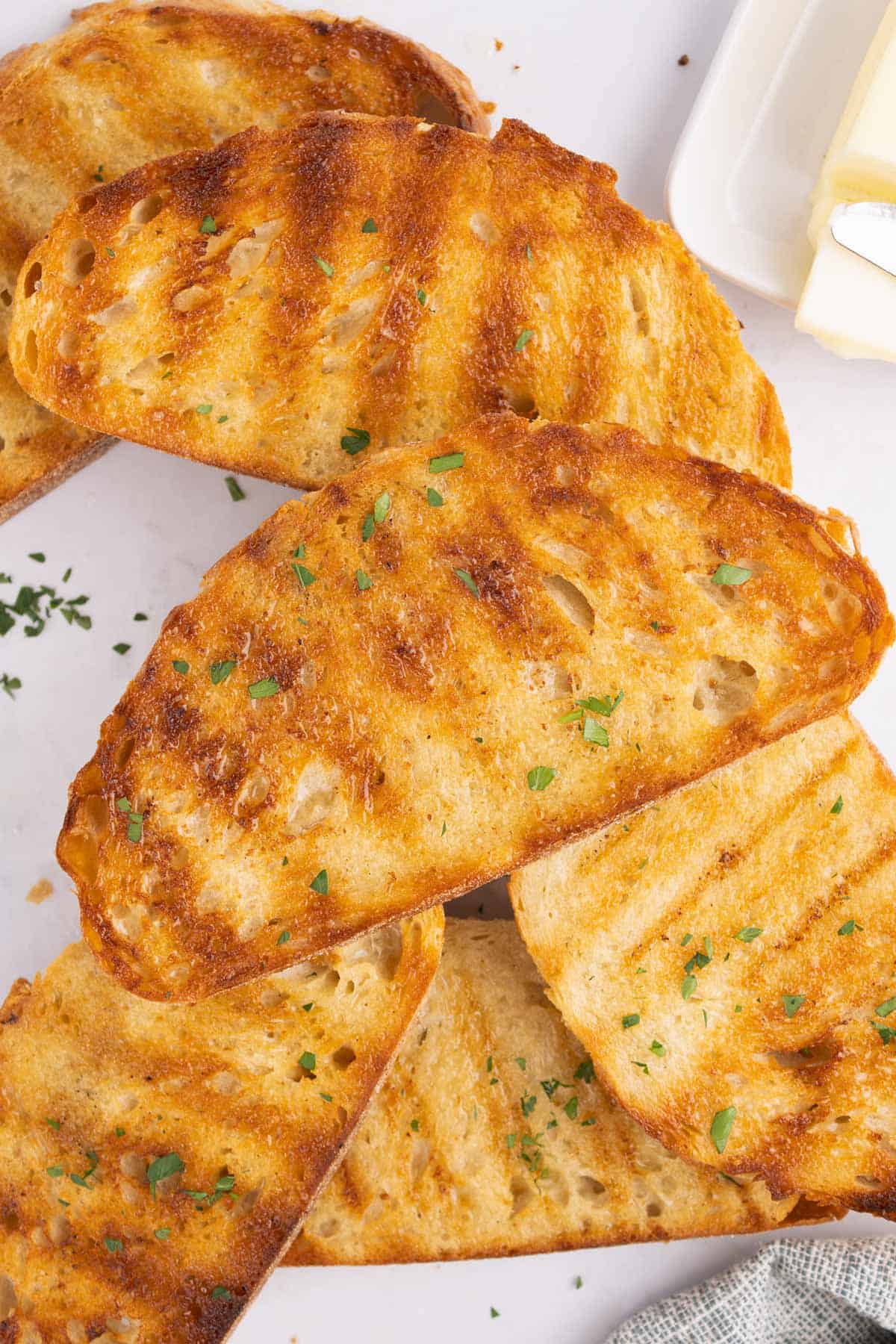 Grilled bread arranged in a pile topped with herbs.
