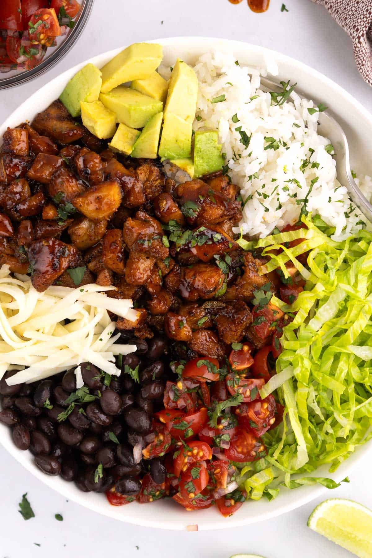 A dish with an array of veggies, beans, cheese, rice, and chicken piled in it.