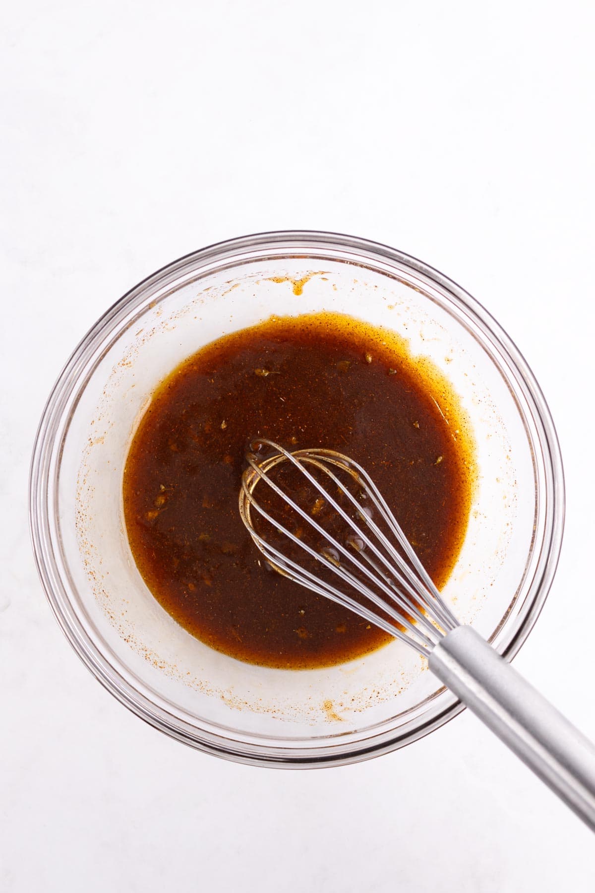 Sauce being mixed in a glass bowl with a whisk.