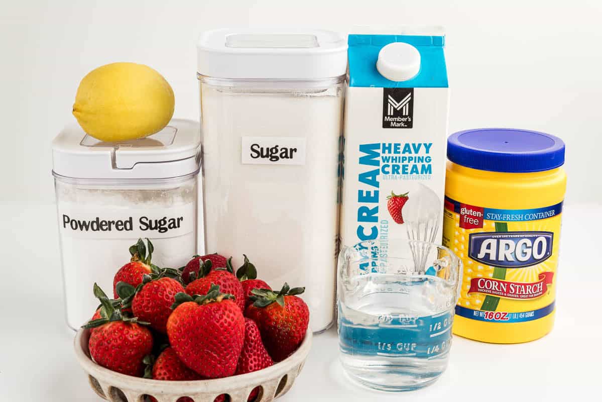A lemon, powdered sugar, strawberries, sugar, water, heavy whipping cream, and corn starch on a white surface.
