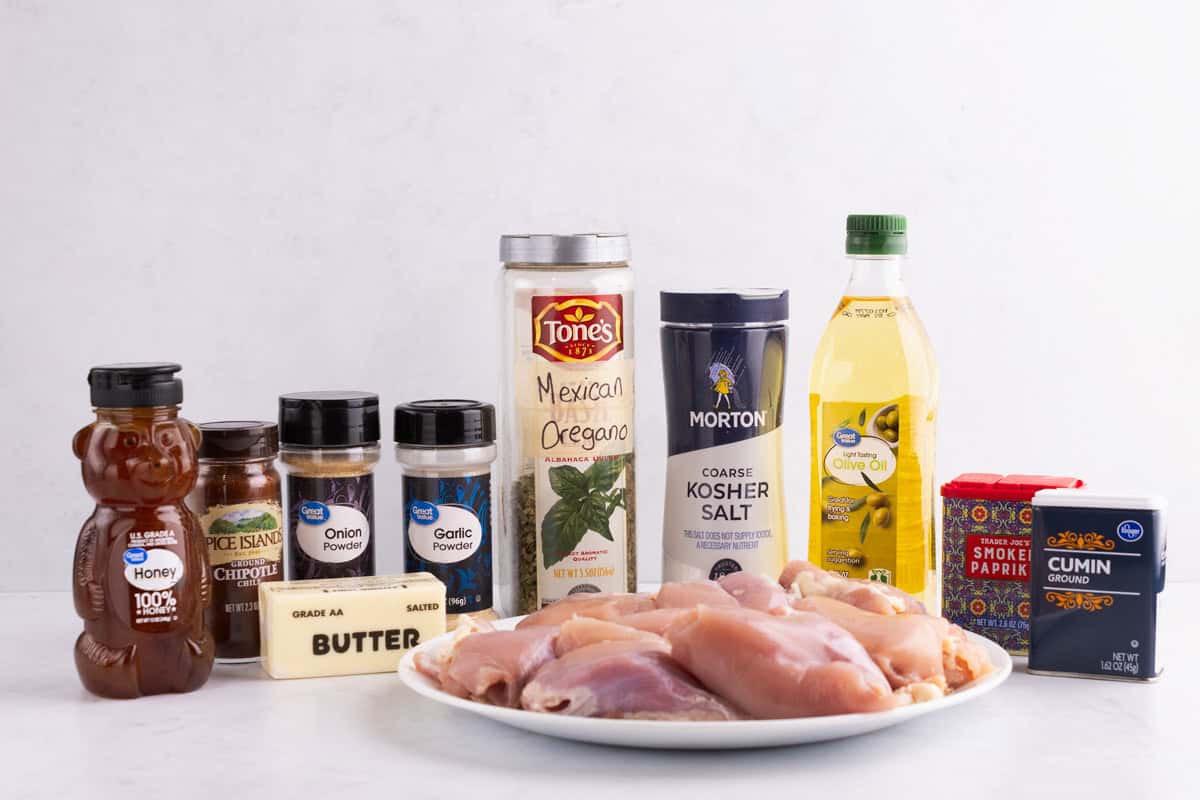 Honey, herbs, butter, salt, oil, and chicken on a white counter.