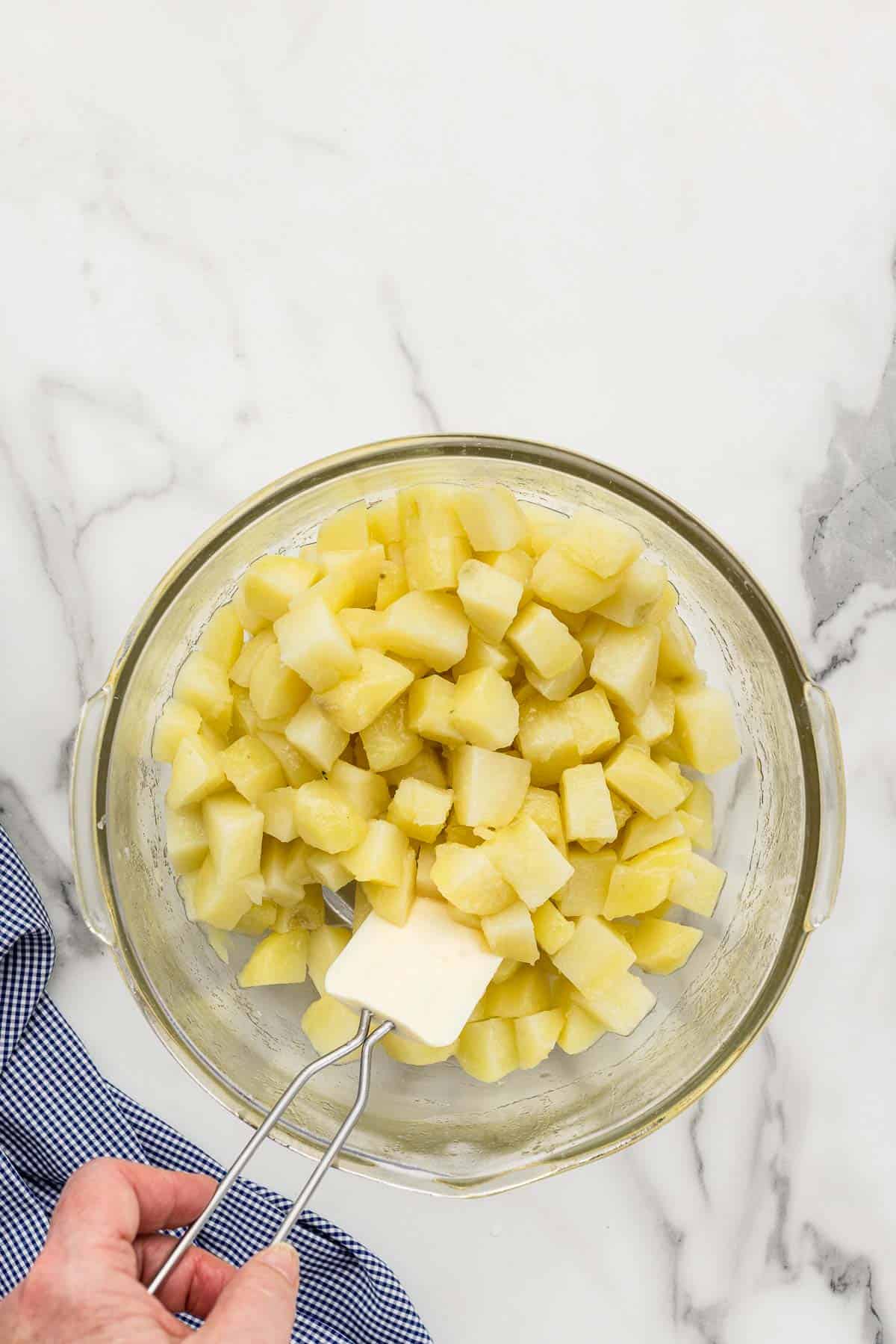 Potatoes in a mixing dish with a spatula.