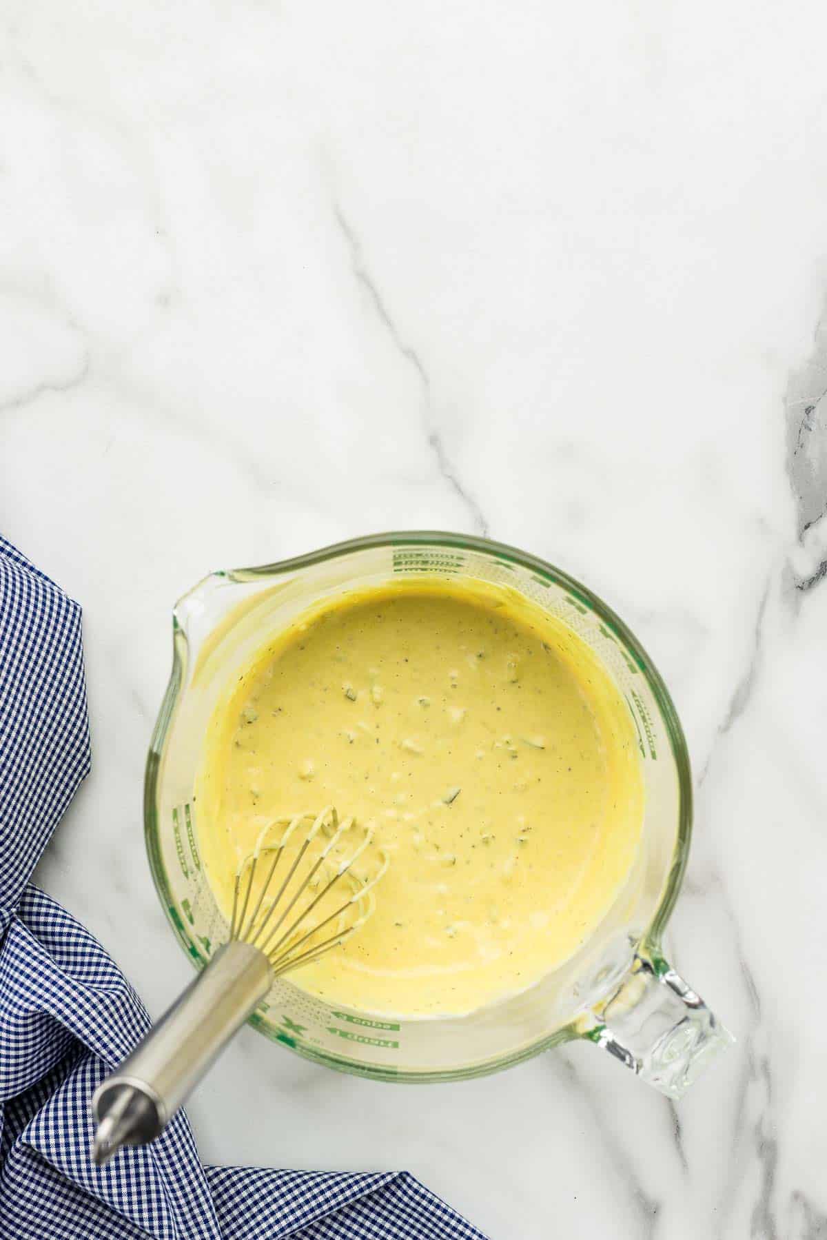 Potato salad dressing being mixed in a measuring glass with a whisk.