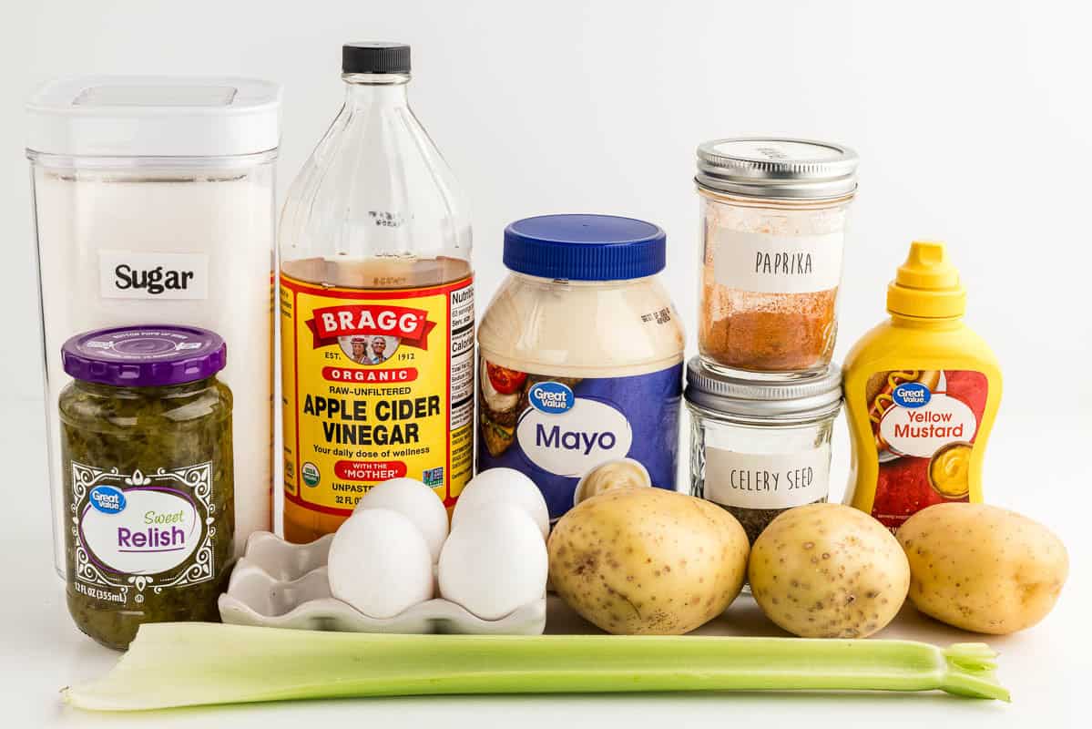 Sugar, relish, celery, apple cider vinegar, eggs, potatoes, mayo, paprika, celery seed, and mustard on a white countertop.
