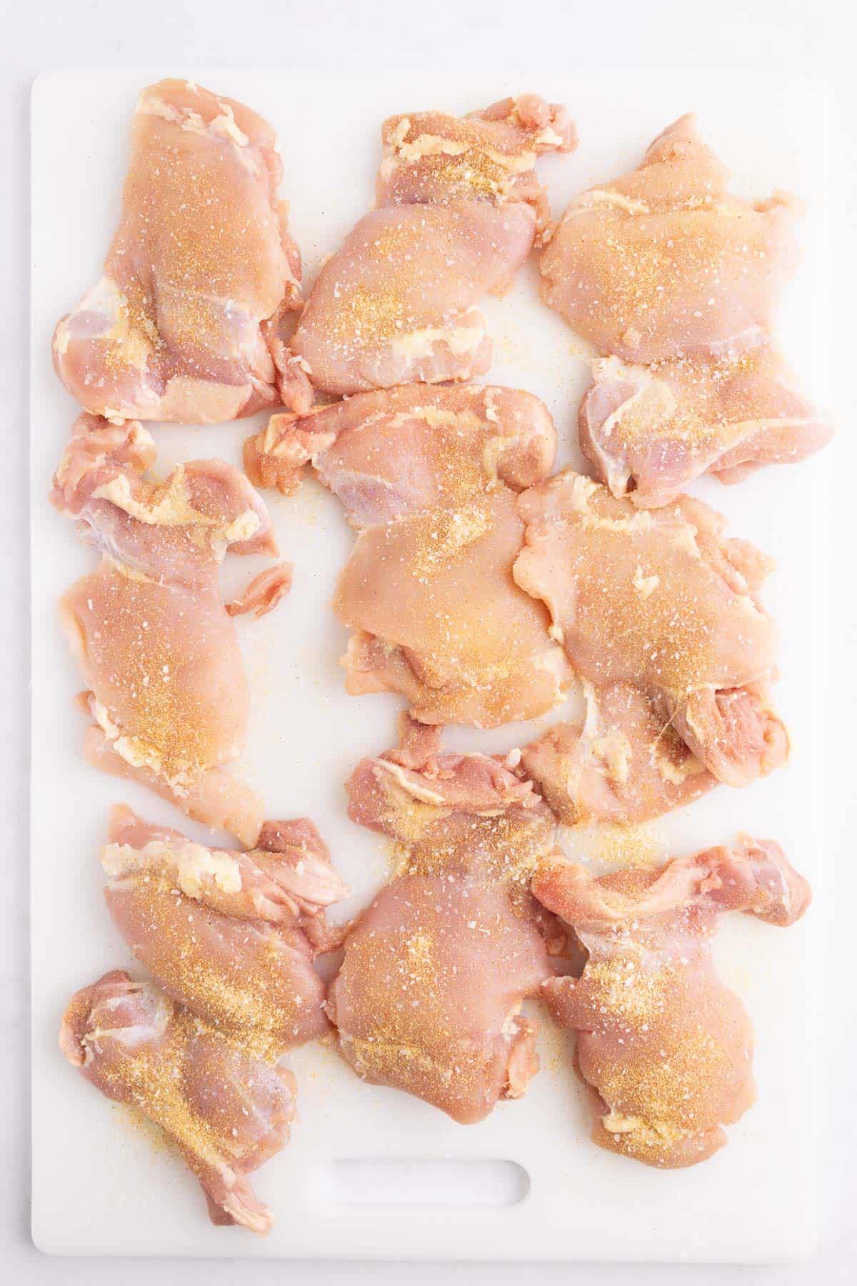 Raw chicken seasoned and laid out on a cutting board.