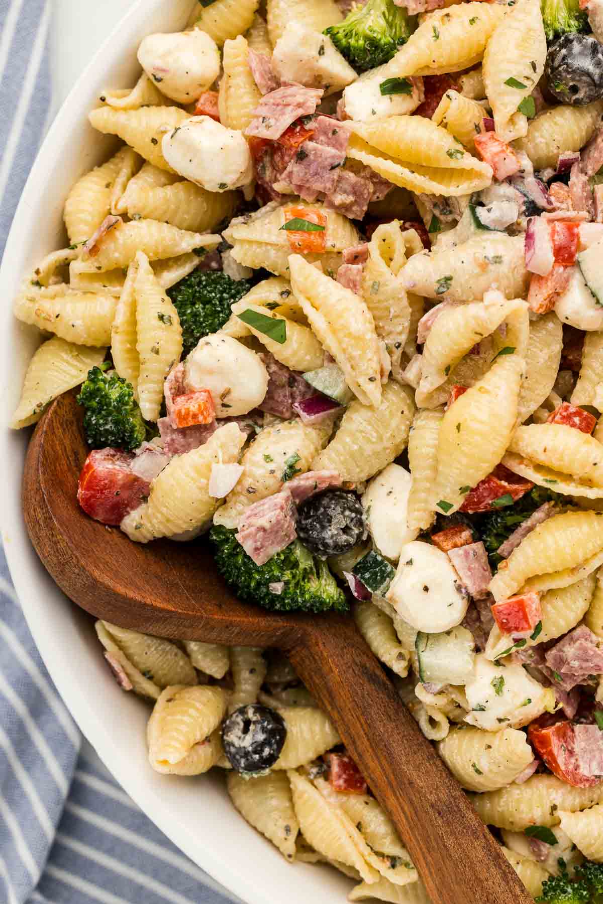 A wooden spoon tucked to the side of a bowl of pasta salad.