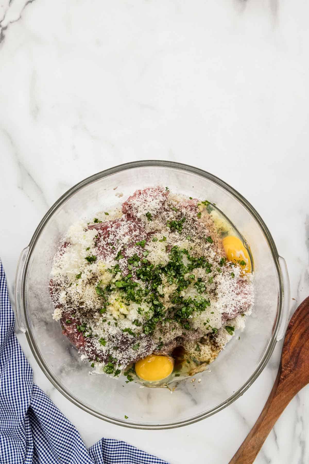 Unmixed ingredients for meatballs in a glass dish.