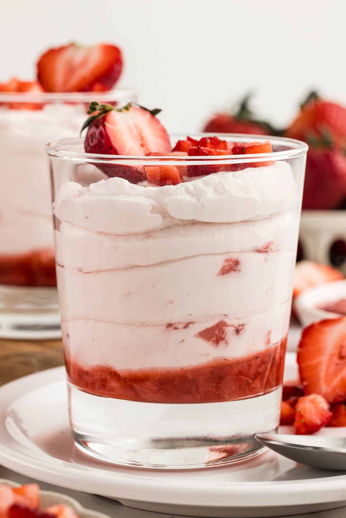 A cup of strawberry mousse on a white plate with a spoon.